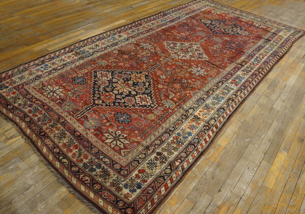 Long low-pile rug featuring complex red, navy, and cream geometric designs on distressed wood floors.
