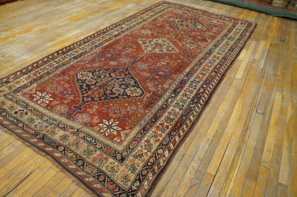 Terracotta patterned rug featuring blue, cream, and multicolor geometric borders covers worn wooden flooring.