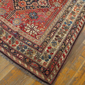 Intricate red, navy, and cream patterned rug corner displaying geometric borders on wood flooring.