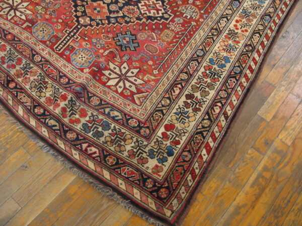 Intricate red, navy, and cream patterned rug corner displaying geometric borders on wood flooring.
