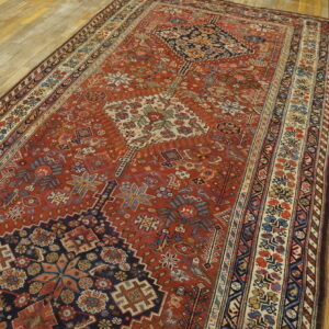 Rust red geometric rug with blue and cream patterns rests on light, distressed wood plank flooring.