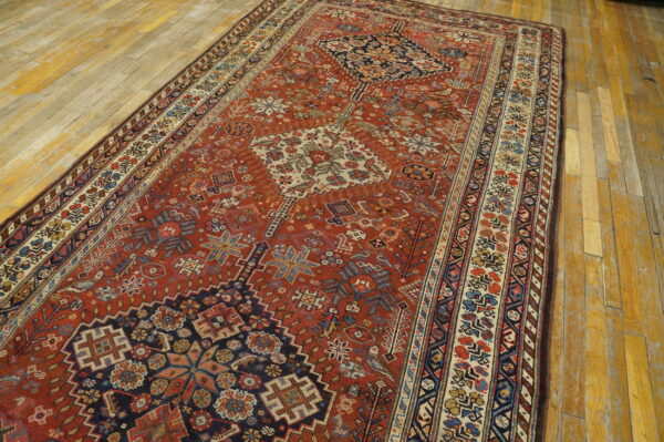 Rust red geometric rug with blue and cream patterns rests on light, distressed wood plank flooring.