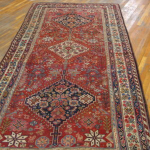 Intricate red and navy geometric rug featuring stylized motifs centered on distressed wood flooring.