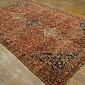 Red and navy low-pile rug with dense floral patterns and diamond accents on distressed wood flooring.