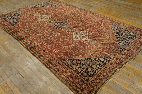 Red and navy low-pile rug with dense floral patterns and diamond accents on distressed wood flooring.