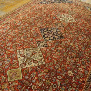 Low-pile red rug with dense traditional patterns, offset navy and cream squares, displayed on wood planks.