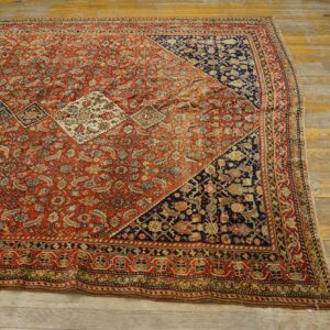 Detailed red patterned rug with blue corner motifs lying diagonally across aged, pale wooden floorboards.