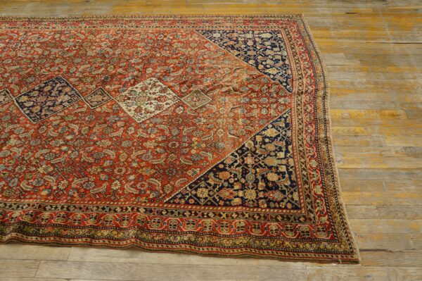 Detailed red patterned rug with blue corner motifs lying diagonally across aged, pale wooden floorboards.
