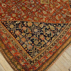 Intricate traditional rug pattern featuring deep red and navy blue fields and a detailed border on wood flooring.