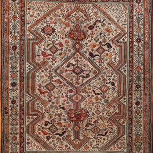 A detailed rug featuring an ivory field covered in dense red, blue, and earth-toned tribal geometric motifs.