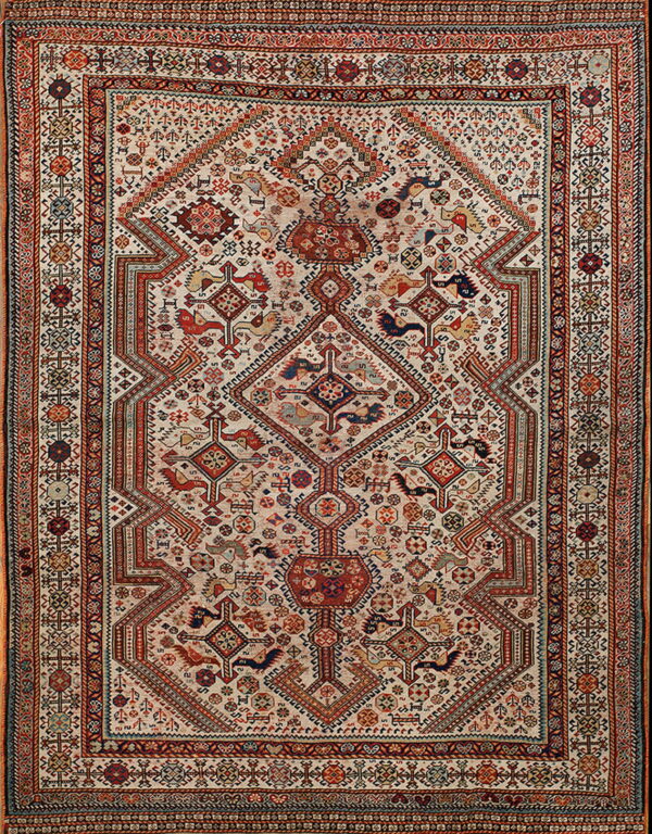 A detailed rug featuring an ivory field covered in dense red, blue, and earth-toned tribal geometric motifs.