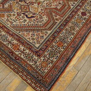 Low-pile rug with complex beige, red, and blue tribal patterns resting on light wooden floorboards.