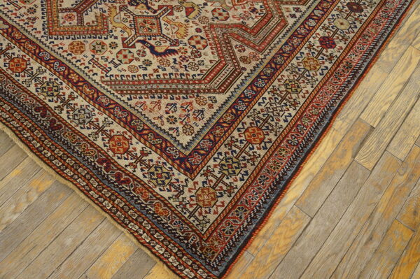 Low-pile rug with complex beige, red, and blue tribal patterns resting on light wooden floorboards.