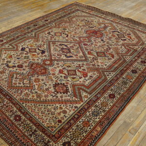 Stepped medallion rug with intricate red, blue, and yellow tribal patterns on a light tan ground over wood planks.