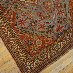 Geometric patterned rug in red, blue, and yellow features a low pile on light wooden floorboards.