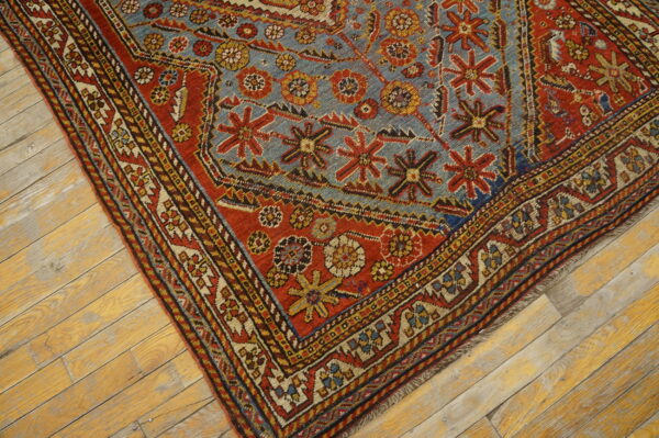 Geometric patterned rug in red, blue, and yellow features a low pile on light wooden floorboards.