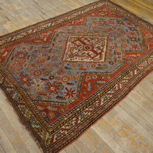 Rust red and slate blue geometric rug featuring a central medallion on distressed light wood floors.