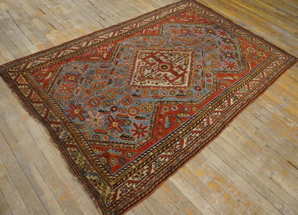 Rust red and slate blue geometric rug featuring a central medallion on distressed light wood floors.