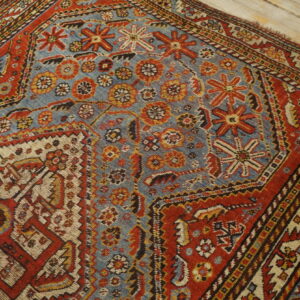 Low-pile rug with geometric patterns in faded blue, rust, and cream, resting on light wood planks.