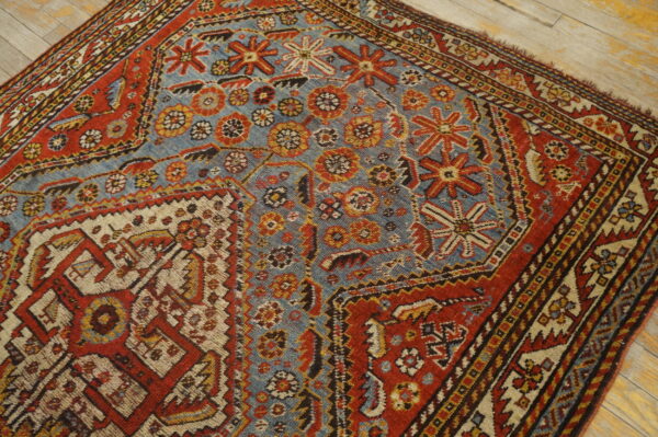 Low-pile rug with geometric patterns in faded blue, rust, and cream, resting on light wood planks.
