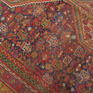 Low-pile rug detail showing dense geometric tribal patterns in deep red, navy, yellow, and green.