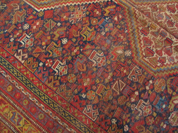 Low-pile rug detail showing dense geometric tribal patterns in deep red, navy, yellow, and green.