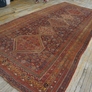 Long red and blue geometric rug with repeating medallions sits on distressed gray wood flooring.