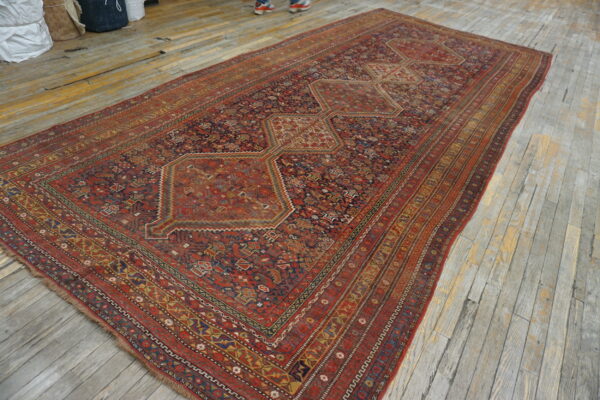 Long red and blue geometric rug with repeating medallions sits on distressed gray wood flooring.