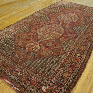 Red and dark brown geometric rug with a central medallion lies angled on yellow wooden floors.