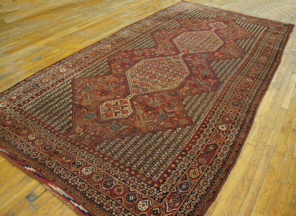 Red and dark brown geometric rug with a central medallion lies angled on yellow wooden floors.