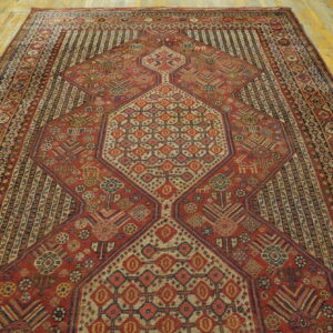 Red rug with detailed geometric patterns and multiple borders centered on a worn wooden floor.