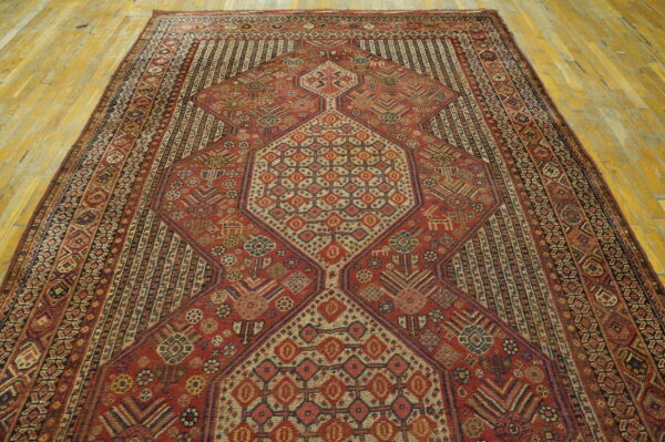 Red rug with detailed geometric patterns and multiple borders centered on a worn wooden floor.