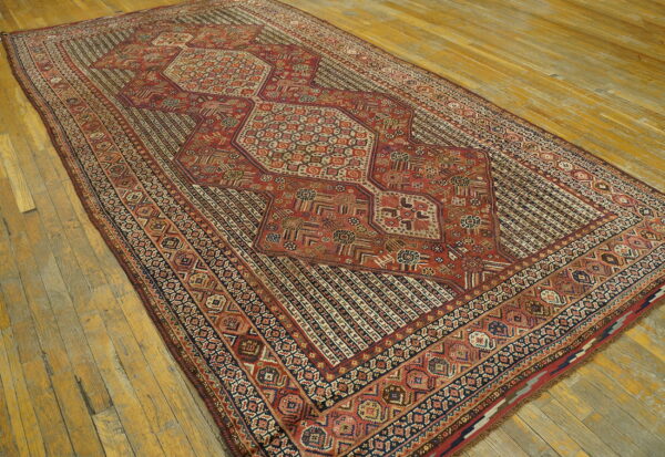 Red and navy geometric rug with a segmented central medallion lying on wide, weathered wood floors.