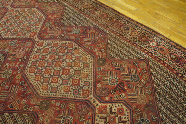 Geometric patterned rug in shades of red, cream, and black resting on light yellow wood plank flooring.