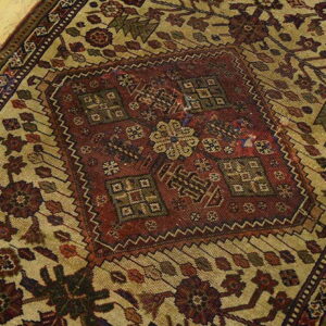 Close view of a tan and dark red rug with complex medallion and botanical patterns on light wood flooring.