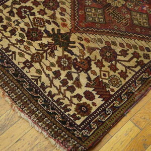 Beige, red, and brown traditional rug corner with visible fringe rests on light wooden plank flooring.