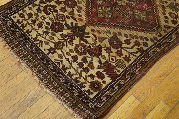 Beige, red, and brown traditional rug corner with visible fringe rests on light wooden plank flooring.