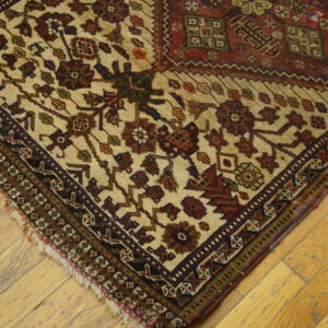A low-pile rug with geometric and stylized florals in cream, red, and dark green rests on light wood plank flooring.