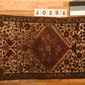 Small rug with a red geometric medallion and stylized floral designs on a beige field over wood flooring.