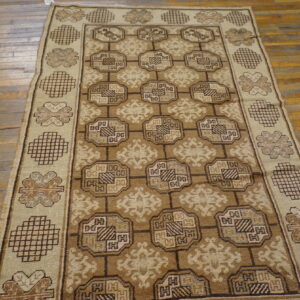 Tan and brown geometric area rug displayed on distressed wood plank flooring.
