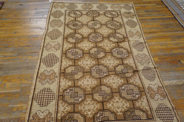 Tan and brown geometric area rug displayed on distressed wood plank flooring.