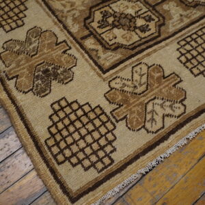 A tan and brown geometric rug with fringes rests on distressed wood planks.