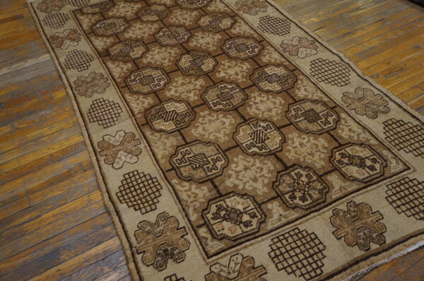 Neutral brown rug featuring a central geometric grid pattern and beige patterned border on distressed wood floors.