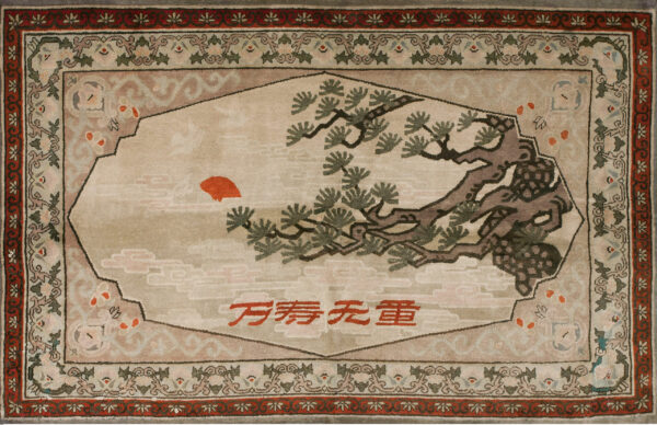 Beige pictorial rug featuring a pine branch, red sun, and red script surrounded by a geometric floral border.