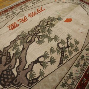 A beige rug features a large brown tree design, red Chinese characters, and detailed red and green borders.