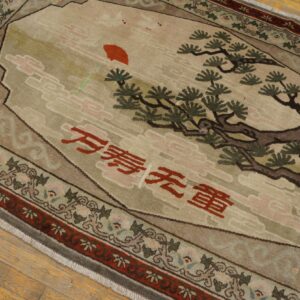 Tan and green pictorial rug featuring a tree, red sun, and script on a light wood floor.