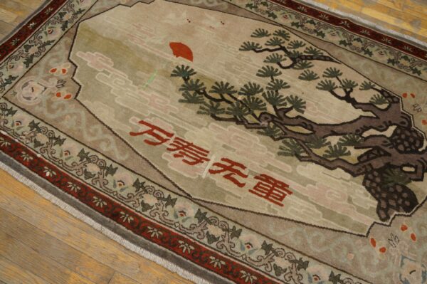 Tan and green pictorial rug featuring a tree, red sun, and script on a light wood floor.