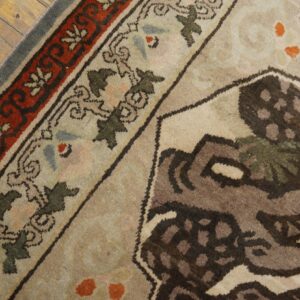 Close-up of a traditional patterned rug in beige, red, and brown on rustic, distressed wood floor.