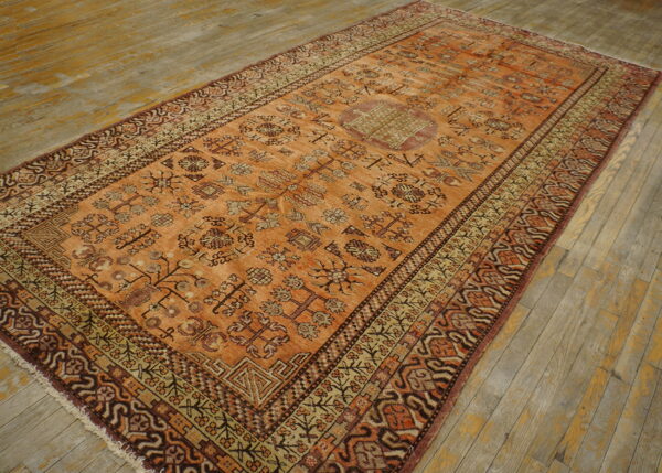 Orange and brown tribal pattern rug with a central medallion lies on distressed wooden floorboards.