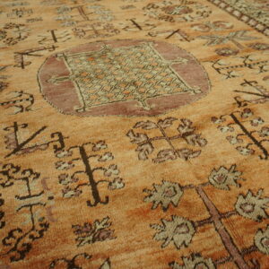 Textured orange rug displays medium pile with geometric and stylized floral tribal motifs in brown and mauve.